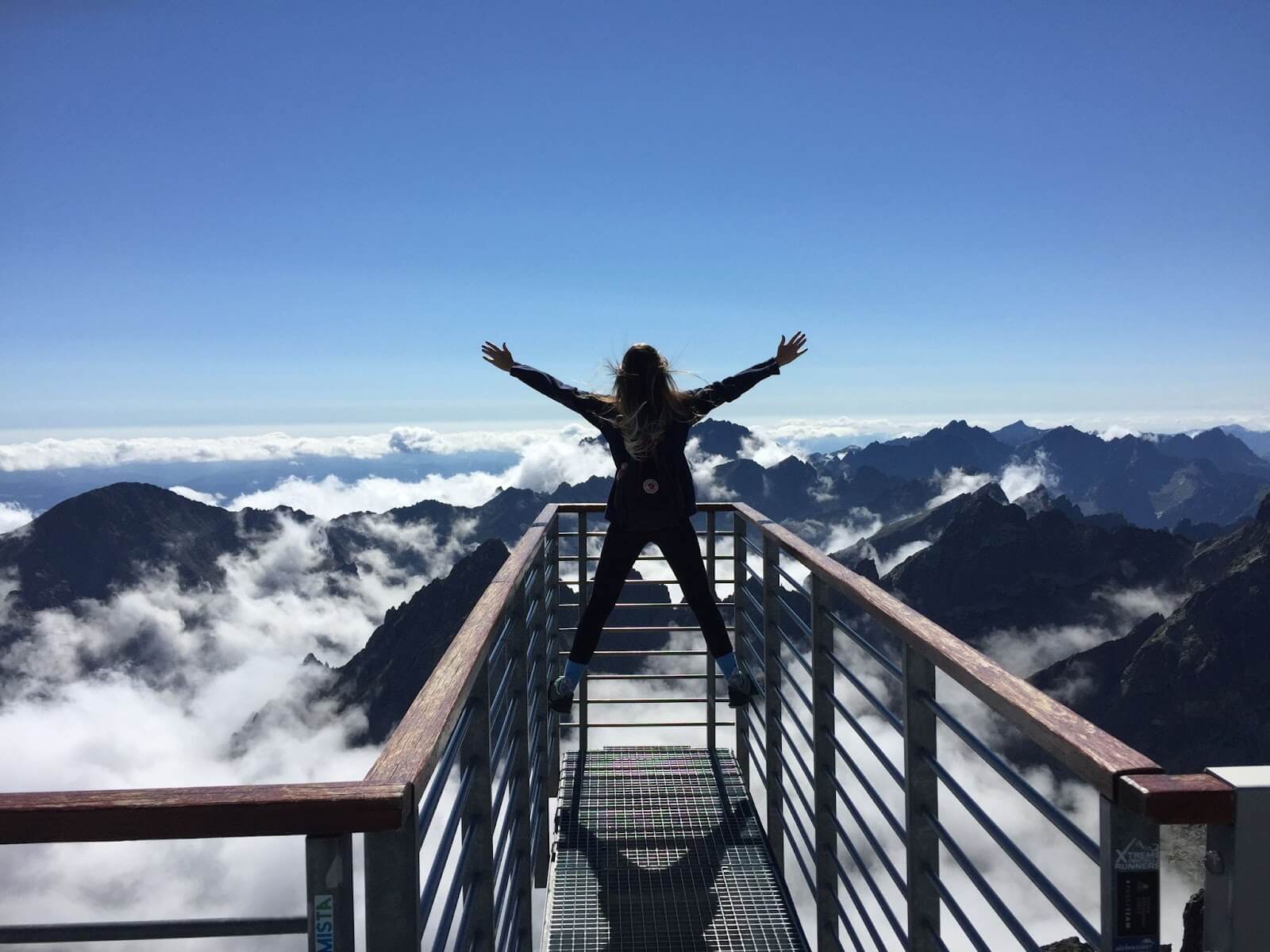 Woman with her arms outstretched, stood on top of a mountain.