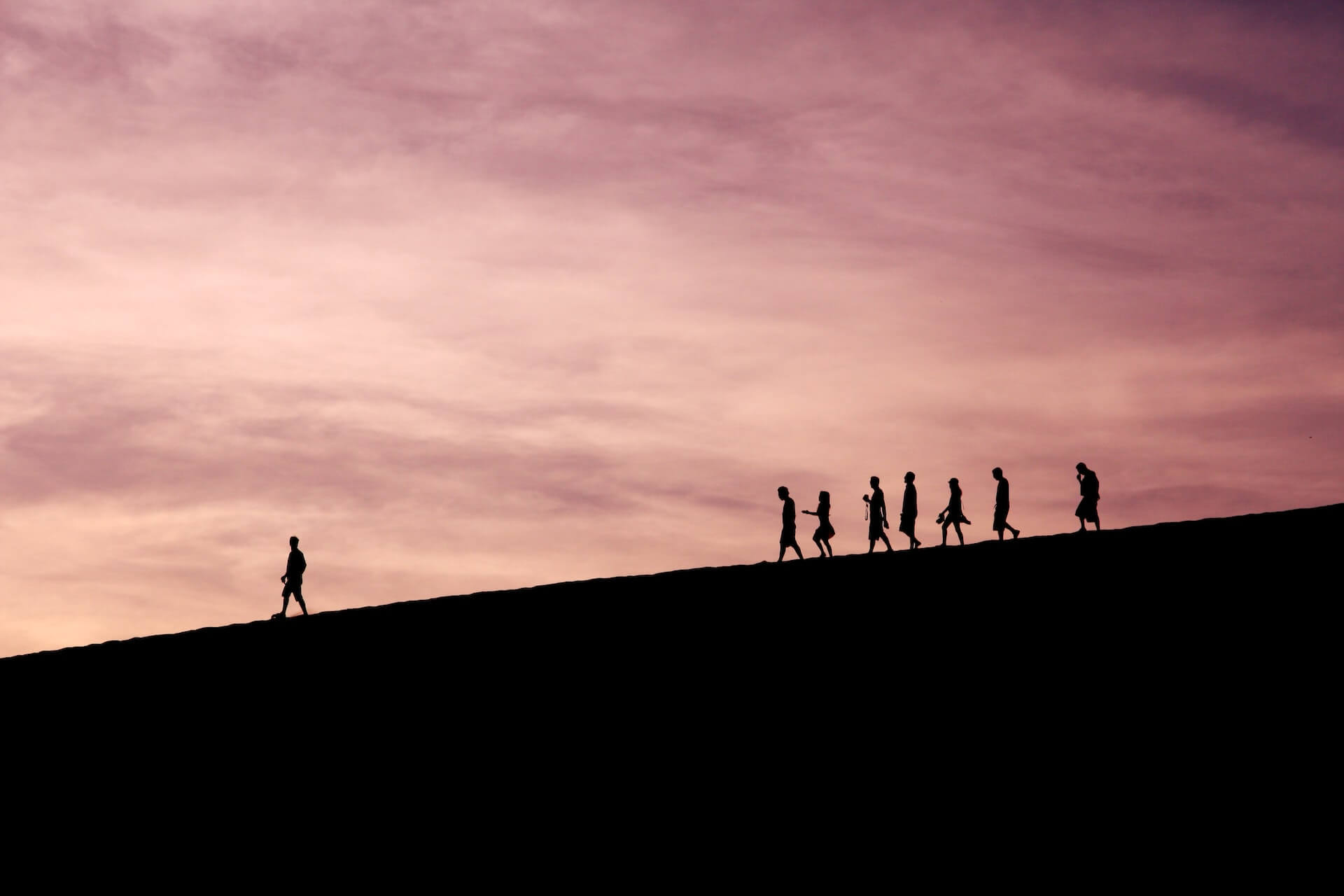 People walking down hill with one person ahead of the group.